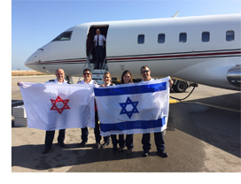 Image of Magen David Adom paramedics holding the MDA flag and Israeli flag in front of a plane that carried them to Nepal, India.